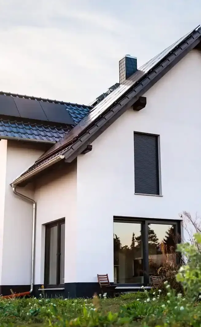 Einfamilienhaus mit weißen Wänden, dunklem Dach und großen Fenstern in einem Garten.