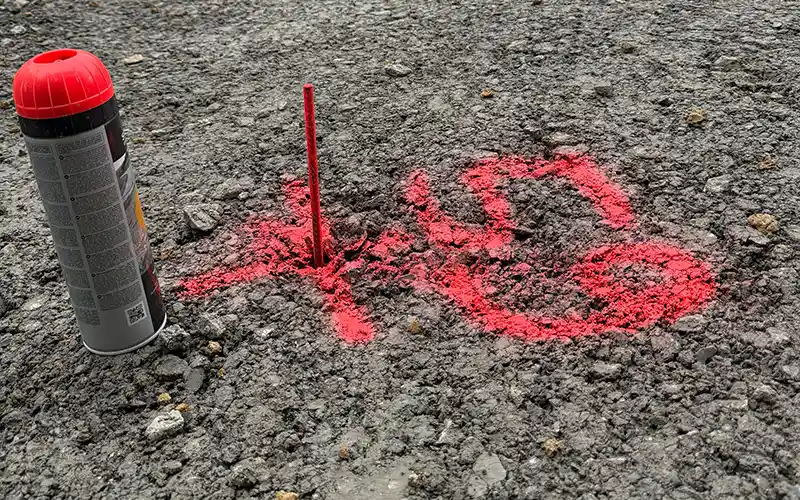 Rote Markierung auf dem Boden mit einer Spraydose und einem Stift in der Nähe.